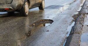 A car driving past a large pothole